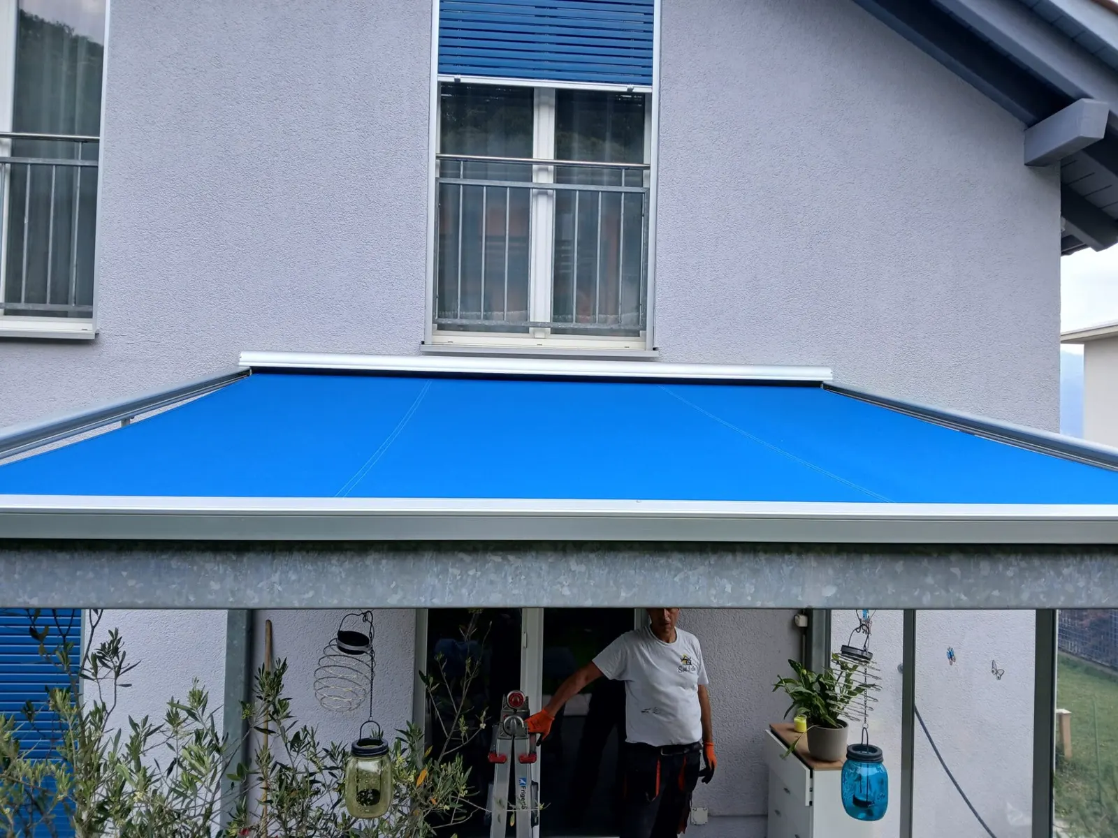 Dopo: la stessa veranda con una tenda blu stesa sopra il tetto in vetro