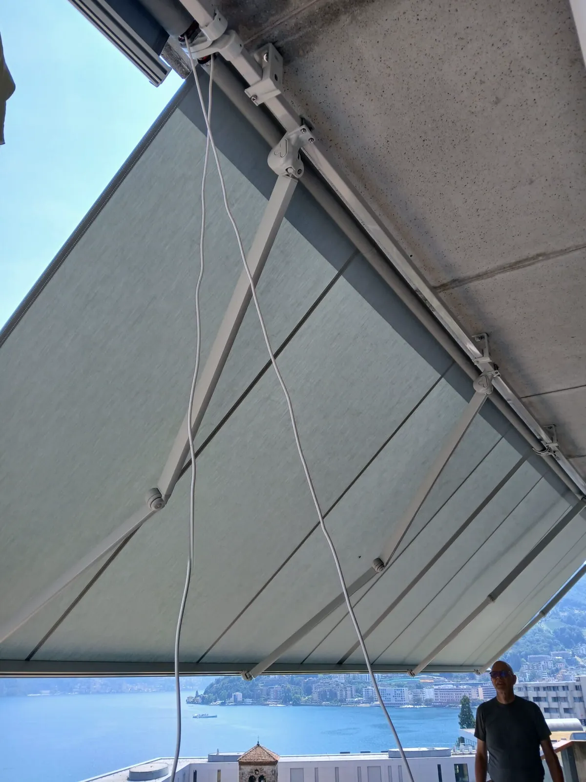 Tenda a bracci estensibili appena posata su una terrazza, con il lago e le colline sullo sfondo